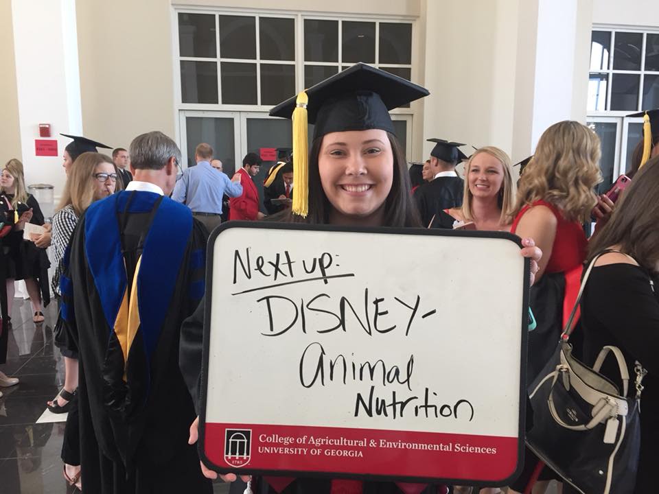 CAES graduate holds sign: "Next up: DISNEY – Animal Nutrition"
